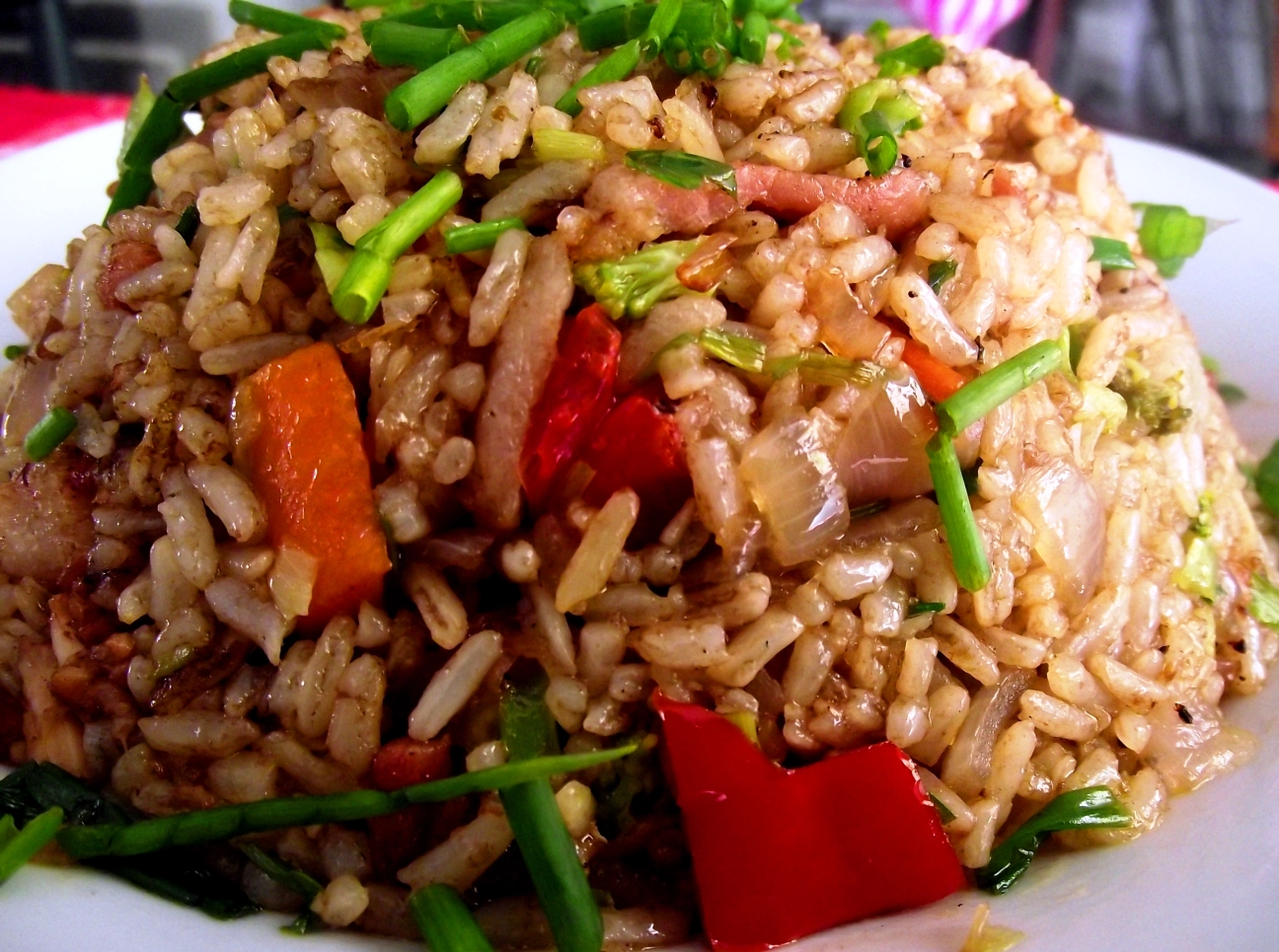 A vibrant plate of Chofan Dominicano featuring colorful fried rice mixed with tender chicken, pork, and shrimp, garnished with green onions and served with a slice of lime on the side. The Dominican-style Chinese fried rice showcases visible vegetables including red bell peppers, peas, and carrots.